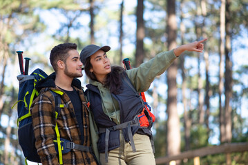 Concentrated couple of young hikers. Caucasian man with beard and woman in cap with big backpacks pointing, discussing route. Hobby, nature, love concept