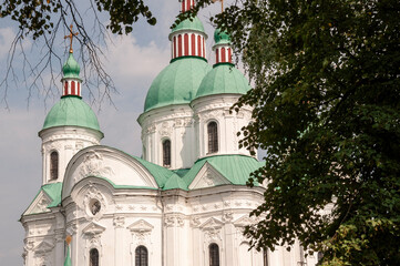 Christian orthodox white church with green domes with gold crosses. Calm blue sky above