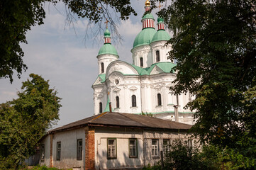 Christian orthodox white church with green domes with gold crosses. Calm blue sky above