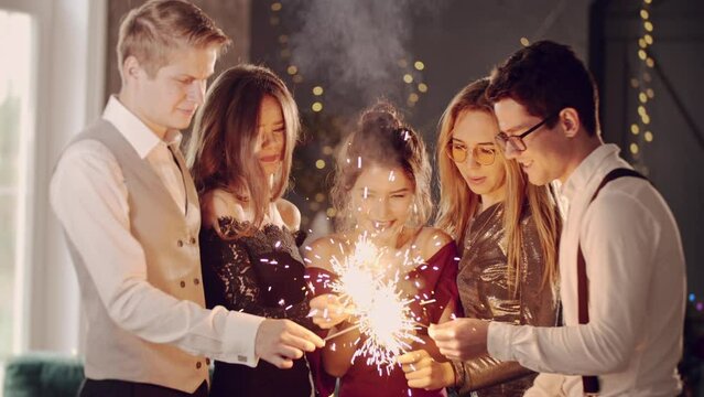 Asian girl and group young college student friends lit light sparkler in hand fireworks, sing and dance together. Woman on Party with people, love friendship relationship and celebration concept.