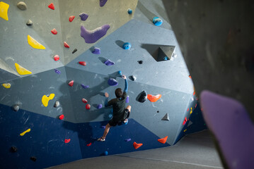 Back view of Caucasian sportsman climbing in gym. Young climber in sportswear training bouldering...