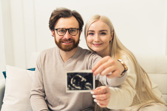 Happy young Caucasian couple showing an ultrasound image to the camera portrait . High quality photo