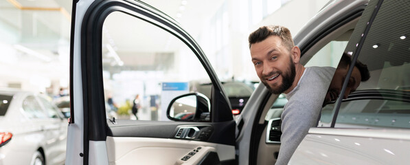 Naklejka premium satisfied customer peeks out from behind the wheel of a new SUV at a car dealership