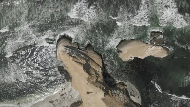 Vertical aerial view of sand sea cliffs and eroded sea stack in Peru