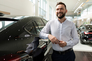 charismatic man with a smile on his face in a car dealership dreams of buying a new car