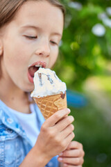 Cute girl liccking and eating italian ice cream cone while resting in park on summer day