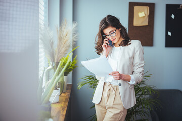 A young business woman standing in a hotel room using a mobile phone. A woman stands in a hotel...