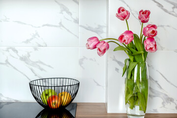 A glass vase with pink tulips and a fruit vase on the kitchen countertop.Home interior.Copy space for text.