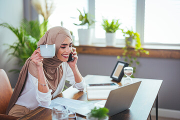A beautiful Muslim woman in a hijab uses a mobile phone for work, communication or learning on a...