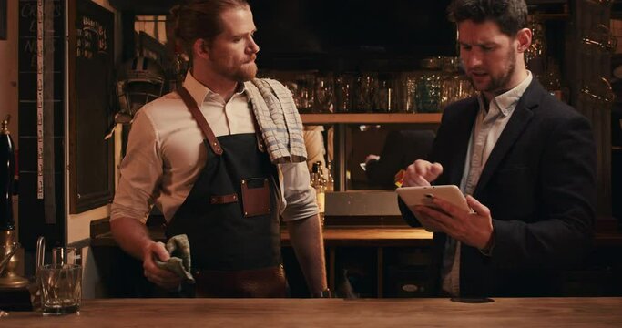 Caucasian male bartender standing with manager holding digital tablet 