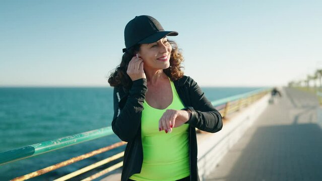 Middle age woman wearing sportswear running and looking stopwatch at seaside