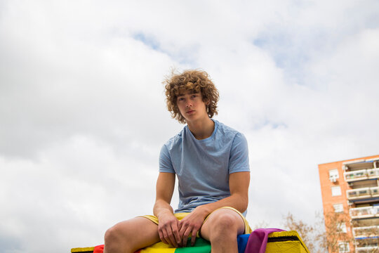 20-something gay man posing sitting on a gay pride flag