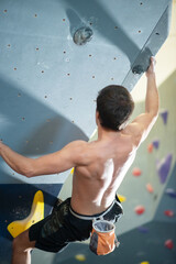 Back view of sportive man training. Sportsman in dark clothes at bouldering wall. Sport, hobby, wellbeing concept