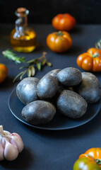 Purple potatoes with tomatoes, garlic, rosemary and olive oil on dark background