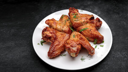 Grilled chicken wings on a plate, on a dark background