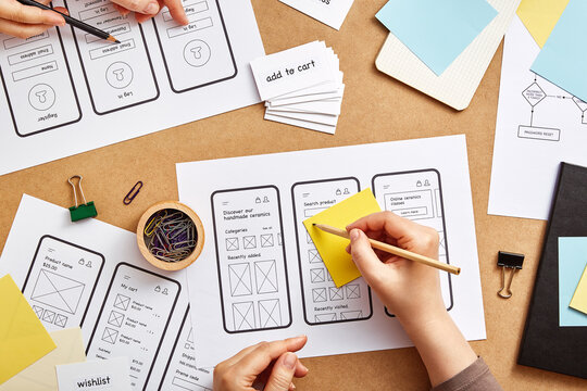 Two web designers working together on mobile responsive website. Flat lay image of numerous app wireframe sketches over product designers desk.