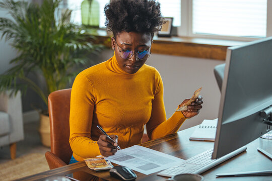 Single young african housewife with many debts feeling stressed, calculating finances, sitting at table with papers, trying to make both ends meet, not able to pay off bills