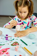 Happy little girl painting, drawing with brush eggs at home.