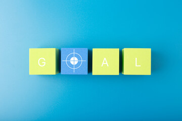 Goal single word and target symbol written on green and yellow geometric figures in a row on blue background