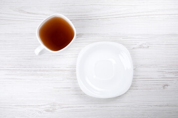 Fototapeta na wymiar Black tea in a white cup and a white plate on a wooden table, close-up