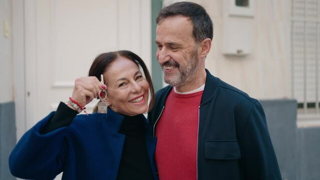 Man and woman couple hugging each other holding key of new house at street