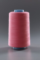Thread for dressmaking, pink colour thread spool on grey surface, yarn for sewing
