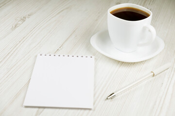 A cup of coffee, a notebook and a white pen on a wooden table. Office work