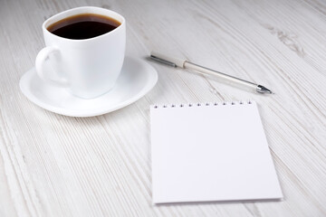 A cup of coffee, a notebook and a white pen on a wooden table. Office
