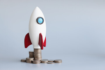 Miniature rocket stand on stack of coins, rocketship as symbol to open business project