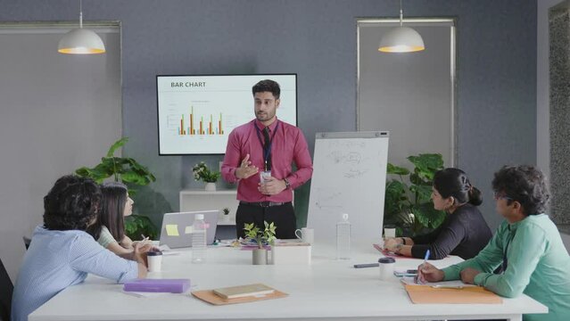 Indian group Businessman Gives Report Presentation to Her Business Colleagues in the Conference Room, She Shows Graphics, Pie Charts and Company's Growth on the Wall TV.