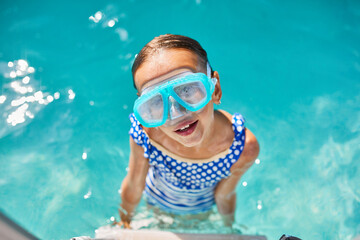 A child in goggles on the steps climbing out of the pool