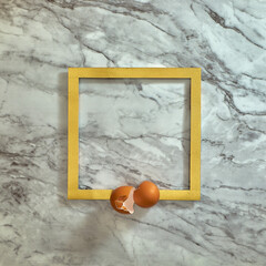 Egg shells on a gold frame. Gray marble background. Text space. Top view. Minimal style. Food, Easter.