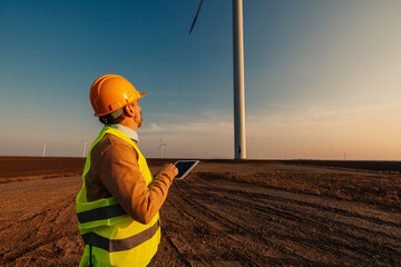 Engineer standing in field with wind turbines and using tablet