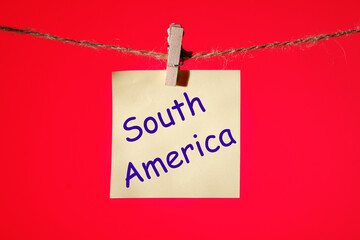 Phrase South America on a yellow sticker on a rope with clothespins on a red background.