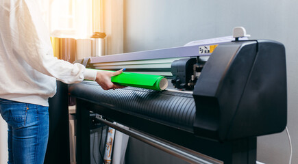 Female hands holding yellow printable material on alarge format printing plotter. Graphic design and  advertising concept.