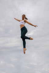 Fototapeta na wymiar Beautiful young woman jumping over cloudy sky. Caucasian woman wearing sportswear. Fitness, wellness concept. Outdoor activity. Copy space. Sky background. Bali