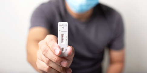 man wearing black t-shirt wear a mask holding Rapid Antigen Test kit (ATK) with Positive result during swab COVID-19 testing, Coronavirus infectious protective concept, copy space