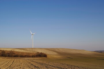 Turbina wiatrowa na wzgórzu wśród pól.