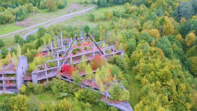 Drone view of abandoned resort building blocks in Kvasy village, Carpathian mountains, Ukraine. Aerial landscape of historical ruined concrete structures inside colorful golden autumn forest.