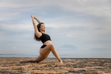 Fototapeta na wymiar Stretching exercise in the morning. Sportive and athletic young female warming up on the beach. Fitness, sport, wellness concept. Healthy lifestyle. Active Caucasian woman workout. Bali