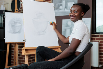 Portrait of student smiling and drawing sketch on canvas during creative art class. Young woman...