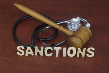 Gavel and stethoscope with letters sanctions on wooden table.