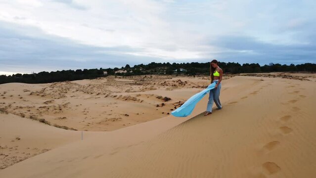 Attractive young woman walking on sandy dunes while her dress is being blown by wind