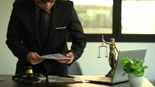 concept of justice and law A male lawyer works in an office with a brass scale goddess on a wooden table. Justice hammer with laptop Legal Concepts and Legal Services