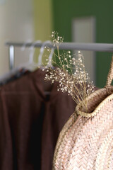 Straw bag, gypsophila flowers and neutral clothes on a clothing rack. Selective focus.