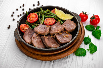 Fried beef tongue with green beans and tomatoes in a pan.