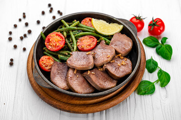 Fried beef tongue with green beans and tomatoes in a pan.