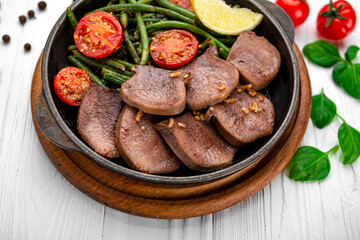Fried beef tongue with green beans and tomatoes in a pan.