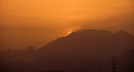 Beautiful evening panoramic landscape with bright setting sun over distant mountain peaks at sunset