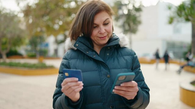 Middle age woman using smartphone and credit card at park